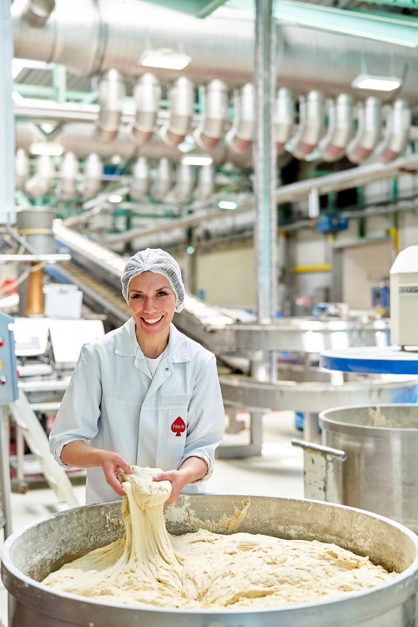 Mitarbeiterin vor einem großen Gefäß mit Pizzateig und hält diesen in der Hand. 
