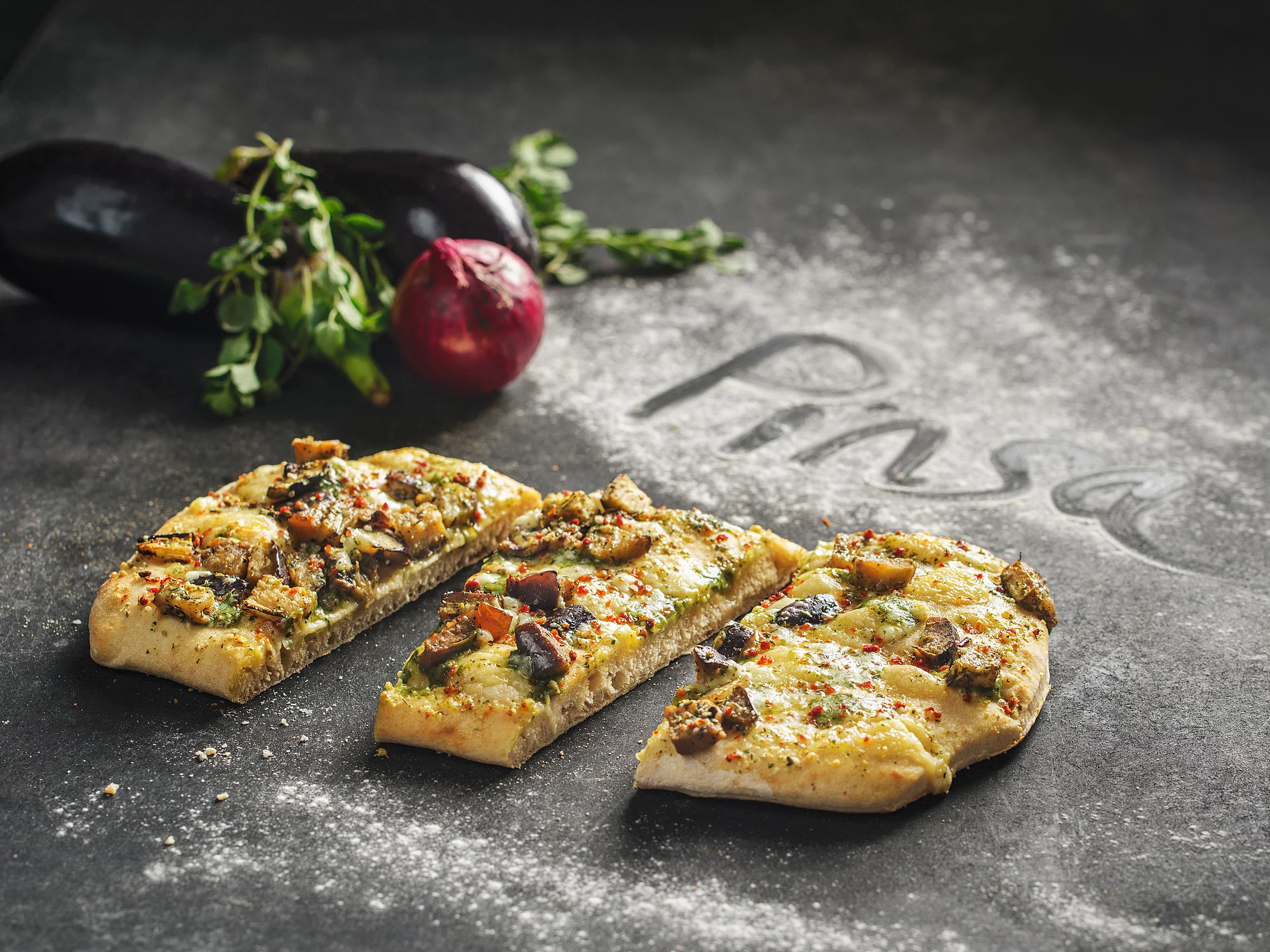 Pizza-Baguette in drei Teile geschnitten, drumherum dekoriert mit Zwiebeln und Basilikum.