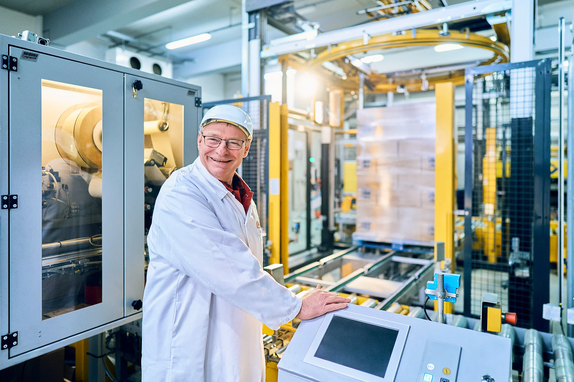 Mitarbeiter steht in Arbeitskleidung an einer Maschine und lächelt.