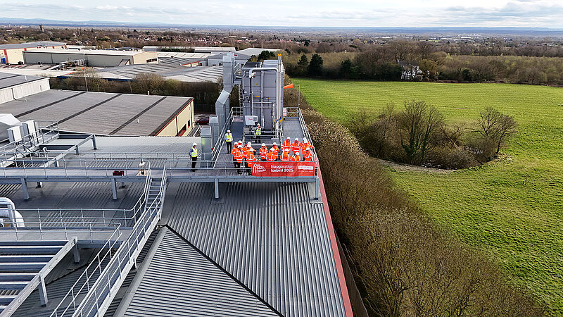 Mitarbeitende in Arbeitsjacken auf einem Steg auf dem Dach der Betriebshallen.