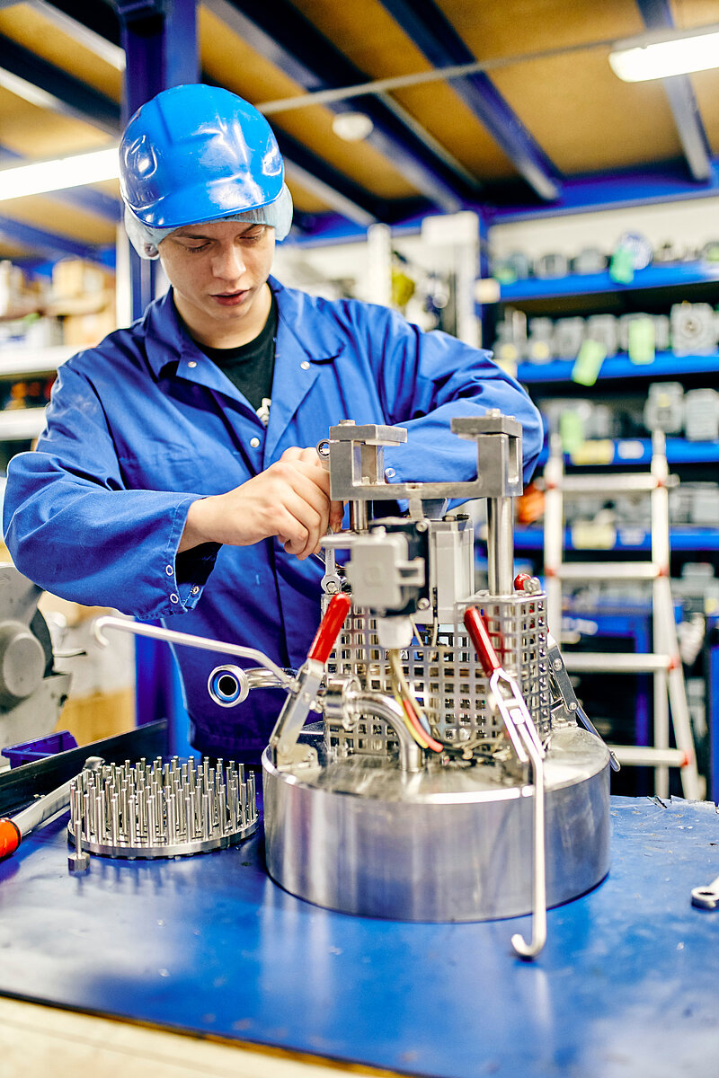 Mitarbeiter in Arbeitskleidung und Helm, am Schrauben an einer Maschine.