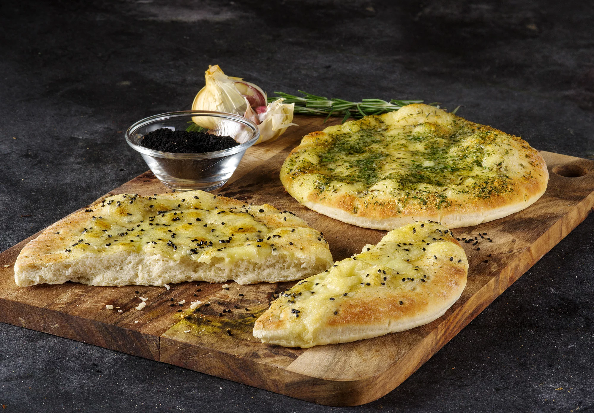 Knoblauch-Pizzabrote auf einem Holzbrett, dekoriert mit einer Schale Olivenöl und Knoblauch.